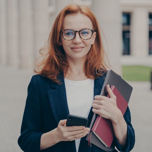 confident-beautiful-red-haired-female-business-consultant-holding-modern-smartphone-and-laptop.jpg