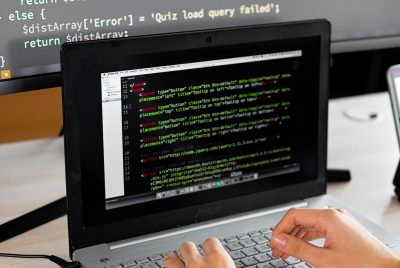 pexels-photo-7988086-7988086 Person coding at a desk with laptop and external monitor showing programming code.